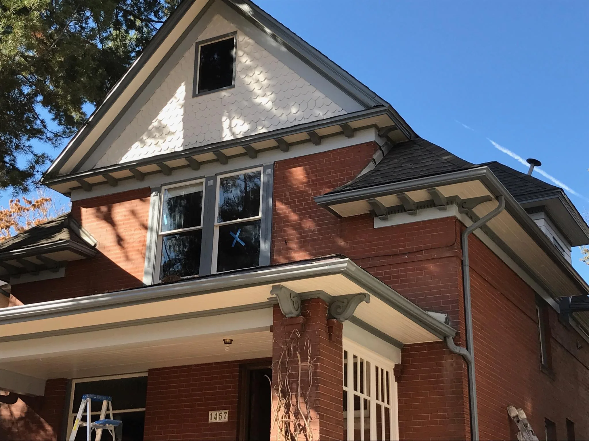 Red brick Victorian with white and green trim being painted, ladder still up mid-job