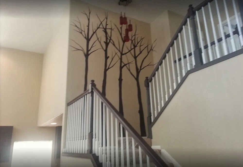 Hand-painted bare tree branch mural climbing a stairwell wall